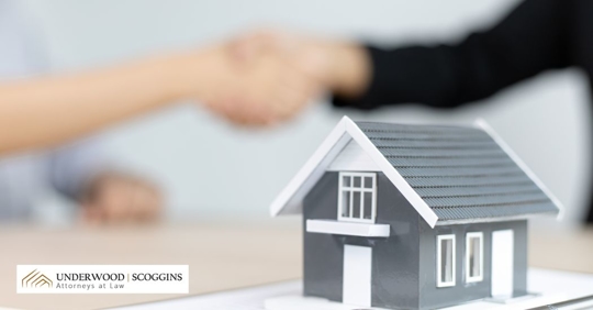 a closeup of a tiny model house with person shaking hands with a real estate lawyer on the background